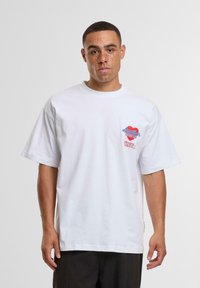 White cotton t-shirt with short sleeves, featuring a colorful graphic on the left chest area and relaxed fit. Smooth texture.