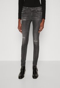 Jeans de mezclilla negra ajustados con ligero desgaste, diseño de cinco bolsillos y cierre de cremallera, combinados con botas negras hasta el tobillo.