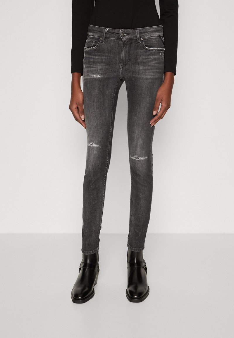 Jeans de mezclilla negra ajustados con ligero desgaste, diseño de cinco bolsillos y cierre de cremallera, combinados con botas negras hasta el tobillo.