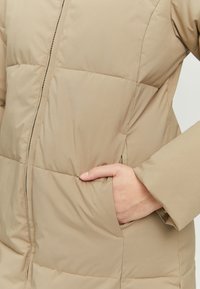 Beige puffer jacket with stitched sections, half-zip closure, and side pockets. Smooth texture with a lightweight, insulated design.