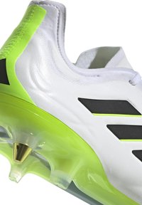Scarpa sportiva bianca con superficie texture, dettagli neri e accenti verde brillante. Presenta una suola trasparente con uno spike dorato.