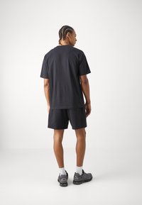 Black cotton short-sleeve t-shirt paired with black shorts, featuring a relaxed fit and a smooth texture. Worn with dark athletic shoes.