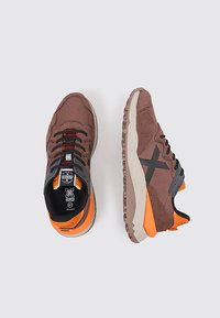 Baskets de sport marron avec des matériaux en mesh et en daim, accents orange, semelles texturées et design de logo noir contrastant sur les côtés.