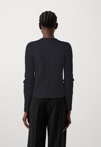 Um suéter escuro e texturizado com mangas longas e decote redondo, combinado com calças largas listradas em preto e branco.