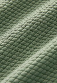 Tissu texturé en vert atténué avec un motif en diamant, présentant un aspect tissé doux et un effet matelassé en relief.