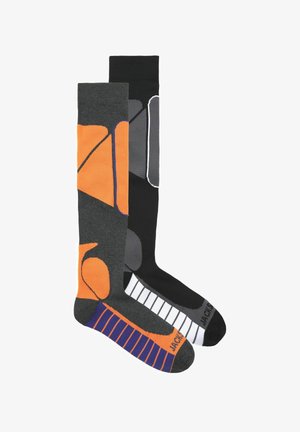 Kneehigh zeķes ar pelēku un oranžu ģeometrisku dizainu vienā un melnām zeķēm ar baltām svītrām otrā, izgatavotas no mīksta auduma.