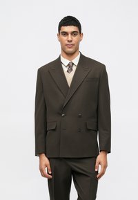 Brown double-breasted suit jacket with notched lapels, two front pockets, worn over a cream knitted vest, paired with a tie and shirt.