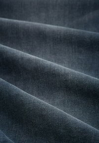 Tela de denim oscuro con una sutil textura, que muestra una superficie lisa y pliegues diagonales, enfatizando su profundo color azul.
