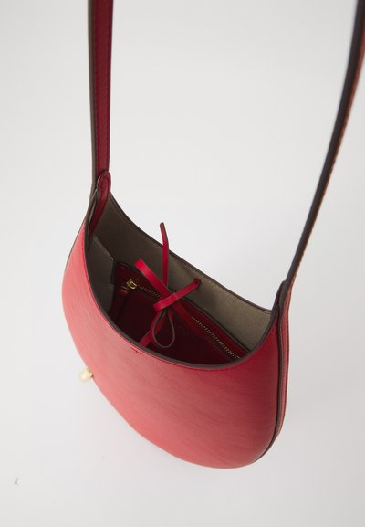 Bolsa de ombro em couro vermelho com uma forma curva, apresentando um bolso com fecho e um interior suave. Alça ajustável e detalhes mínimos em metal.