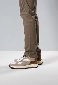 Scarpe sportive beige e bianche con tomaia in camoscio e mesh, punta arrotondata e suola texturizzata. Abbinate a pantaloni marrone chiaro.