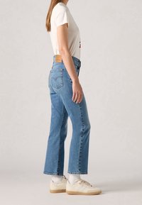 Jean en denim bleu clair avec une coupe droite, taille haute et une étiquette en cuir au dos. Assorti avec un t-shirt blanc et des baskets.
