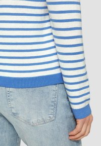Pull rayé bleu et blanc avec un ourlet côtelé bleu, associé à un jean bleu clair avec une poche arrière. Texture tricot douce.