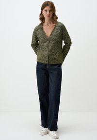 Olijf groene gebreide cardigan met een V-hals, knoopsluiting en een textuurstof. Gecombineerd met donkerblauwe wijde jeans en witte sneakers.