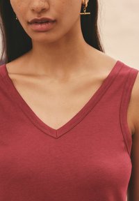 Haut sans manches bordeaux avec un décolleté en V. Tissu en coton doux avec des coutures ton sur ton. Design minimaliste, mettant en valeur le décolleté et les épaules.