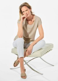 Beige top met korte mouwen en een ronde hals, gecombineerd met lichtgrijze slim-fit broek en beige gevlochten sandalen, zittend op een minimalistische kruk.