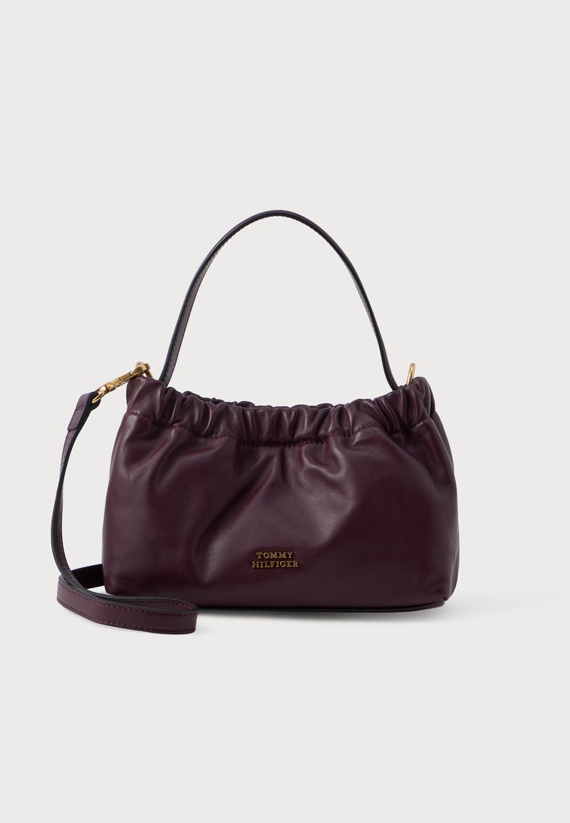 Burgundi odinė rankinė su surinktu dizainu, auksinės spalvos detalėmis ir nuimamu dirželiu; priekyje yra logotipo detalė.