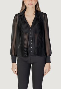 Blusa nera trasparente con pieghe verticali, chiusura a bottoni e maniche lunghe. Presenta un colletto e maniche con polsini, creando una silhouette aderente.