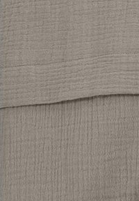 Beige textured fabric with a crinkled pattern, featuring subtle horizontal lines. The surface appears soft and woven.