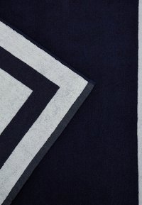 Navyblaues Handtuch mit einem weißen Chevron-Muster. Weiche Textur mit einem dicken, plüschigen Gefühl. Mit gekettelten Kanten und einem kontrastierenden Besatz.