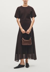 Brown short-sleeve top and a long, layered brown skirt. Holding a small brown leather bag, wearing black mules. Soft textures and flowing design.
