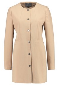 Abrigo beige con cuello redondo, mangas largas, bolsillos delanteros y botones plateados. La tela texturizada crea una apariencia estructurada.