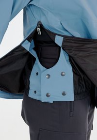 Wasserfeste Jacke mit einer hellblauen Außenhaut und schwarzem Innenfutter, ausgestattet mit Druckknöpfen und einem Reißverschluss zum Schließen.