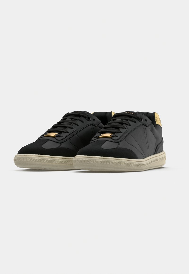 Black leather sneakers with a textured upper, gold accents on the tongue, and a beige rubber sole featuring a patterned edge.