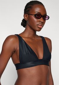 Top bikini nero a costine con design a scollo a V profondo, spalline larghe e tessuto testurizzato. Accentuano una silhouette aderente.