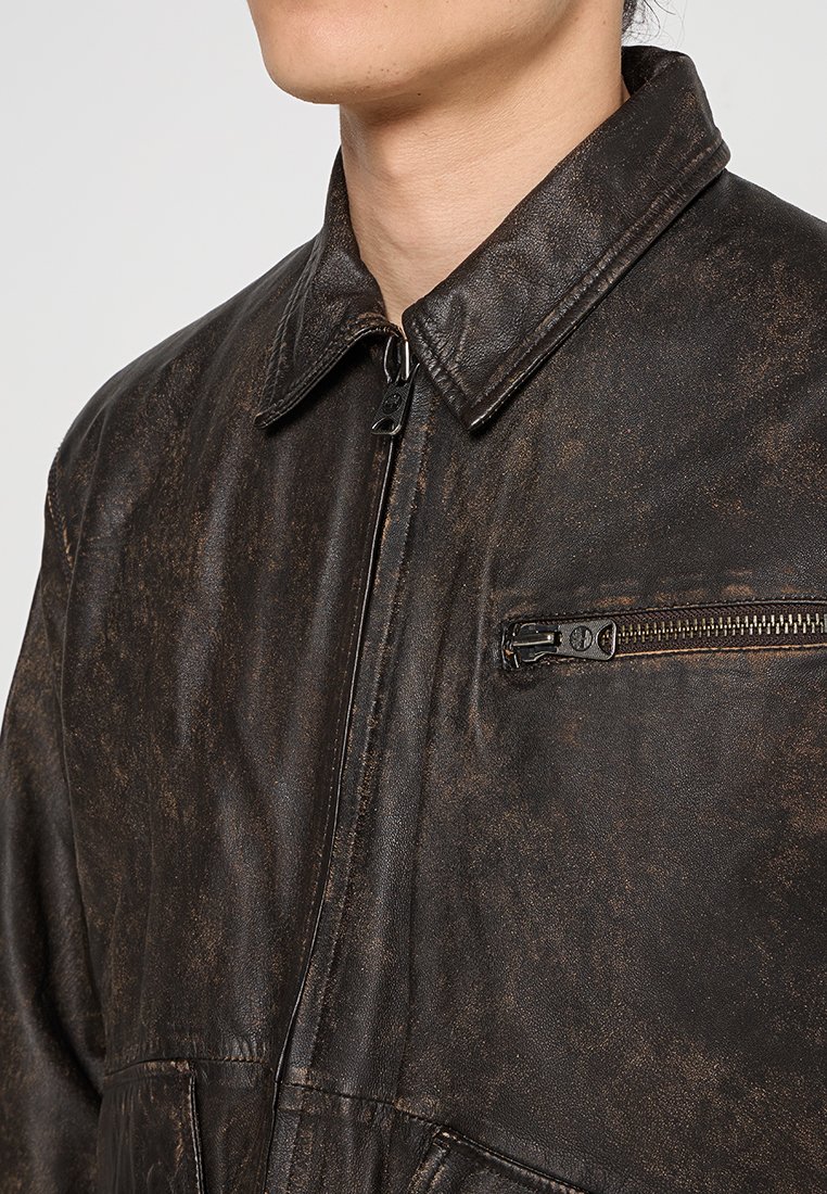 Brązowa skórzana kurtka o zużytej fakturze, z pełnym zamkiem błyskawicznym z przodu i kieszenią na zamek błyskawiczny na piersi. Posiada szeroki kołnierz oraz wzmocnione detale szwów.