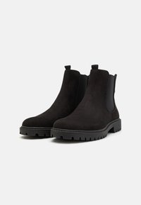 Botines de ante negro con paneles laterales elásticos y tiradores. Presentan una suela de goma gruesa con dibujo para mayor tracción. Diseño de punta redondeada.