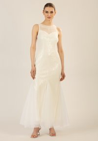 Abito stile sirena con corpetto ricoperto di paillettes, scollatura trasparente e gonna in tulle, di colore crema. Presenta una silhouette aderente e delicati dettagli.