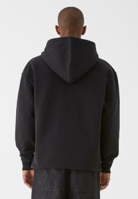 Felpa nera con cappuccio, maniche lunghe, vestibilità larga, materiale morbido, polsini a coste e design semplice senza loghi o motivi visibili.