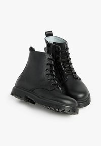Bottines noires en cuir avec une finition lisse, un design à lacets, une semelle en caoutchouc texturée et une languette à l'arrière pour un enfilage facile.