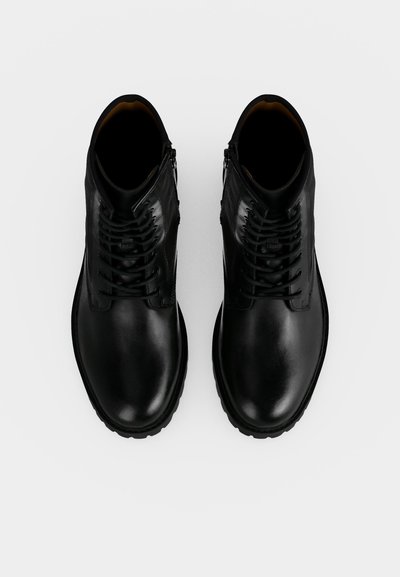 Paire de bottines en cuir noir avec lacets et fermetures éclair latérales vues de dessus sur fond blanc.