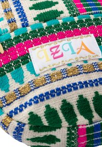 Tessuto intrecciato con accenti verdi, rosa, blu e dorati. Presenta un motivo decorativo e un'etichetta bianca con testo multicolore "IZIA."