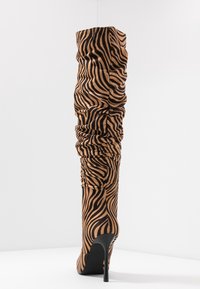 Bota de muslo con estampado de cebra en tela suave, con detalles fruncidos, tacón de aguja negro y diseño de punta estrecha.
