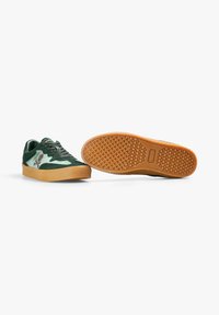 Zapatillas de ante verde con suela de goma, con un patrón texturizado en la suela exterior y un logotipo en el lateral. Cintas en verde a juego.