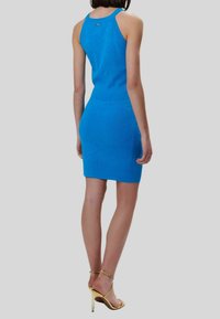 Abito lavorato a maglia blu con una silhouette aderente, schiena a scoop, motivo testurizzato e lunghezza a metà coscia, abbinato a tacchi alti dorati con cinturini.