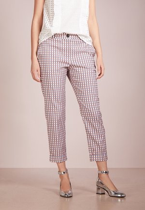 Žena v zkrácených kalhotách s kostkovaným vzorem v bílé, hnědé a fialové barvě, doplněných stříbrnými botami na blokovém podpatku s kotníkovým páskem a bílým tílkem bez rukávů.