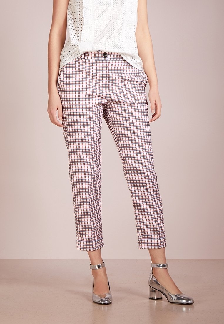 Femme portant un pantalon court à carreaux blancs, marron et violets, associé à des chaussures à talons blocs argentées avec bride à la cheville et un haut blanc sans manches.