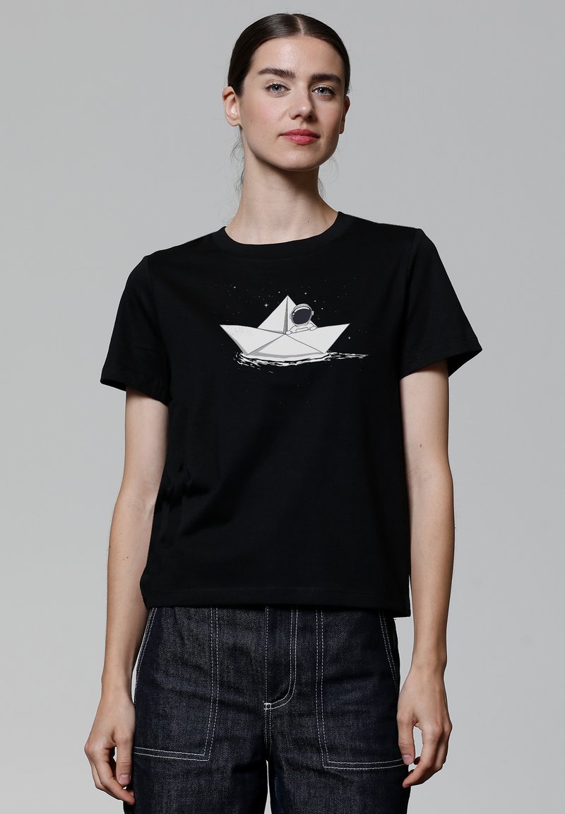 Zwart katoenen T-shirt met een witte afbeelding van een papieren boot met een astronaut binnenin, tegen een sterrenachtige achtergrond. Korte mouwen, ronde halslijn.