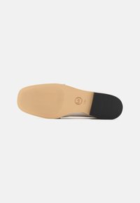 Zool van een schoen met een beige rubberen basis, met een gestructureerd grippatroon. Zwarte hakaccent aan de achterzijde.