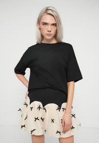 Musta oversize t-paita lyhyillä hihoilla yhdistettynä kermaiseen tüllihameeseen, jossa on aaltoileva helma ja mustat nauhat.