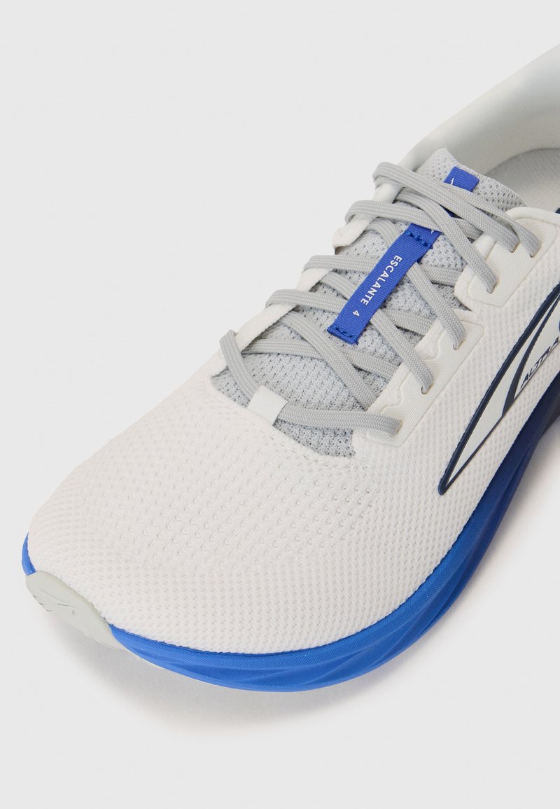 Zapatilla de running blanca de malla con acentos grises y suela azul. Presenta un upper texturizado, cordones estándar y una etiqueta de marca en la lengüeta.