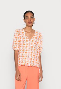Blusa floral em tecido leve com flores laranja e rosa sobre um fundo branco, com mangas bufantes e decote em V. Botões da parte superior visíveis.