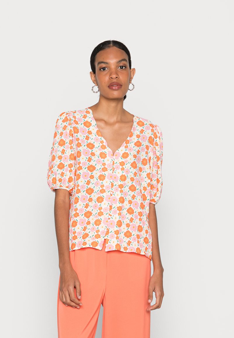 Blusa floral em tecido leve com flores laranja e rosa sobre um fundo branco, com mangas bufantes e decote em V. Botões da parte superior visíveis.