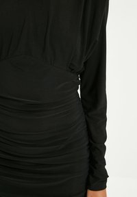 Robe noire à manches longues avec texture froncée, corsage ajusté et tissu lisse. Présente un design drapé en haut et des fronces à la taille.