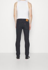 Svarta denimjeans med slim fit, femficksdesign och läderpatch på ryggen. Bärs med en vit linne och svarta sneakers.