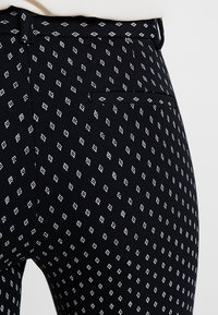 Pantalon en tissu noir avec un motif en diamant texturé blanc. Doté d'une taille et d'un détail de poche à l'arrière. Design lisse et ajusté.