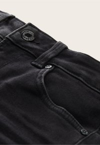 Musta farkkutakki, jossa on etupocketti, nappisuljenta ja tekstuuri kangas. Sisältää näkyvän logon napin varusteessa.